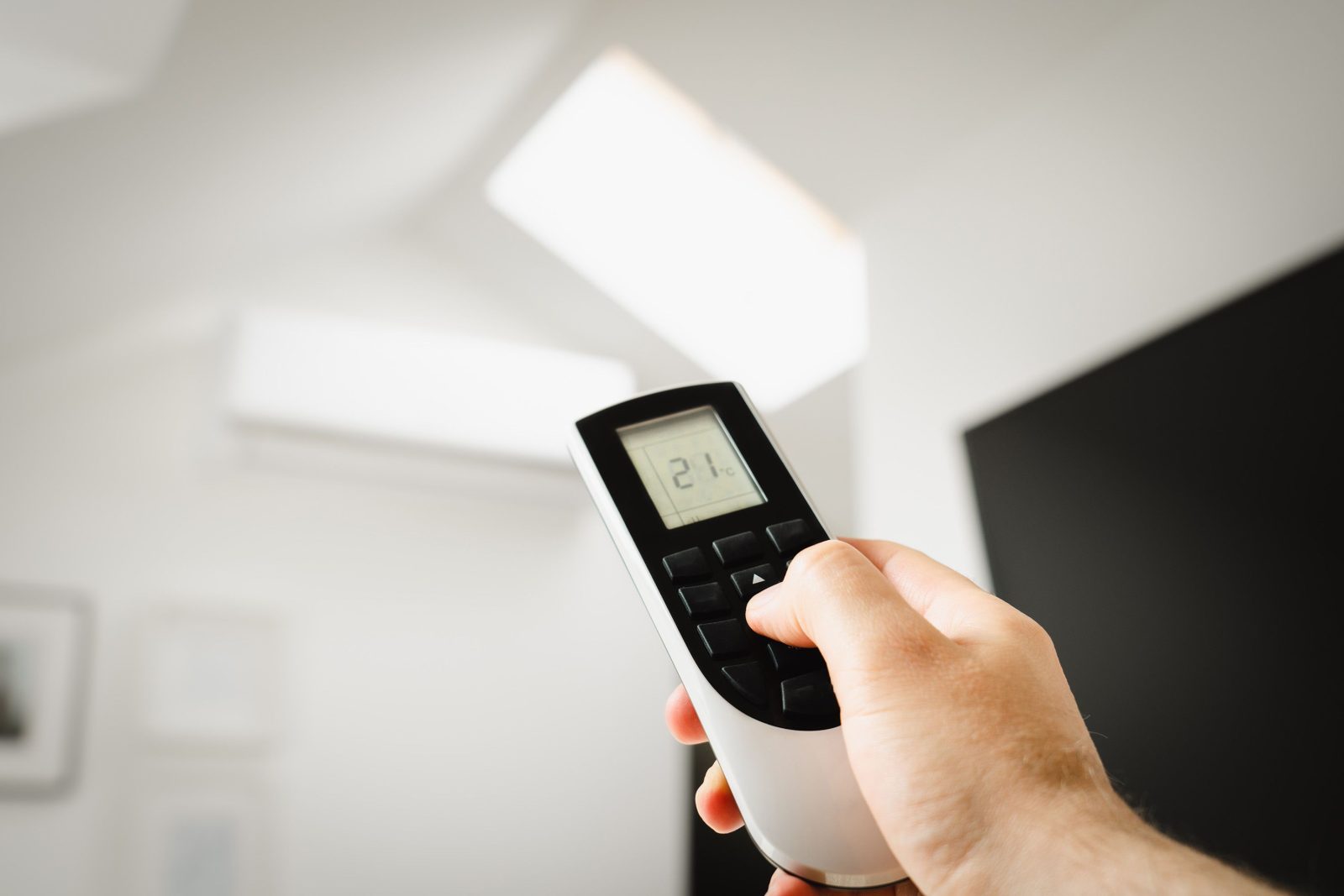 Mano che regola la temperatura a 21 gradi con un telecomando, in un soggiorno